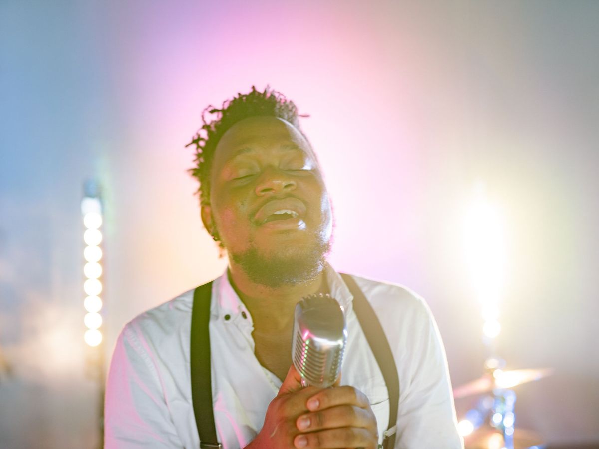 A vocalist singing with eyes closed at a microphone, mid-recording